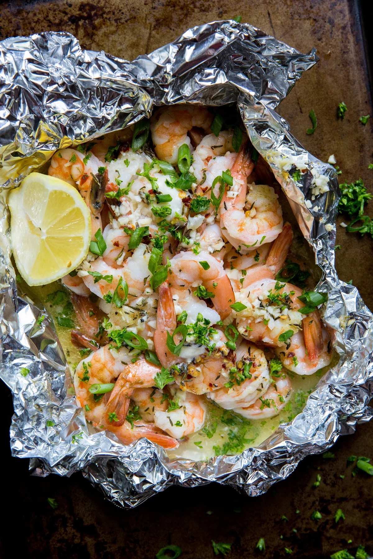 How to Grill Shrimp in Foil Packets. Shrimp foil packet on a baking sheet with fresh herbs sprinkled around.