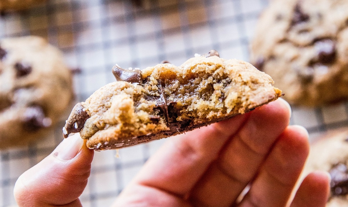 Hand holding a chocolate chip cookie with a bite taken out.