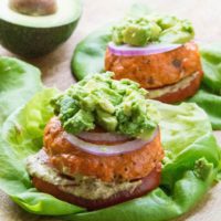 Baked Salmon burgers with mashed avocado on top, red onion, tomato and mustard on a lettuce bun