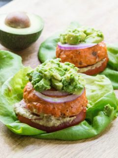Baked Salmon burgers with mashed avocado on top, red onion, tomato and mustard on a lettuce bun