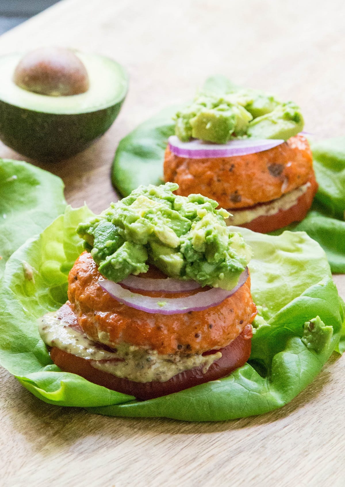 Baked Salmon burgers with mashed avocado on top, red onion, tomato and mustard on a lettuce bun