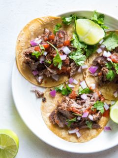 top down photo of beef tacos with red onions, cilantro and salsa on top. Fresh limes to the side.