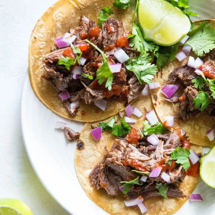 top down photo of beef tacos with red onions, cilantro and salsa on top. Fresh limes to the side.