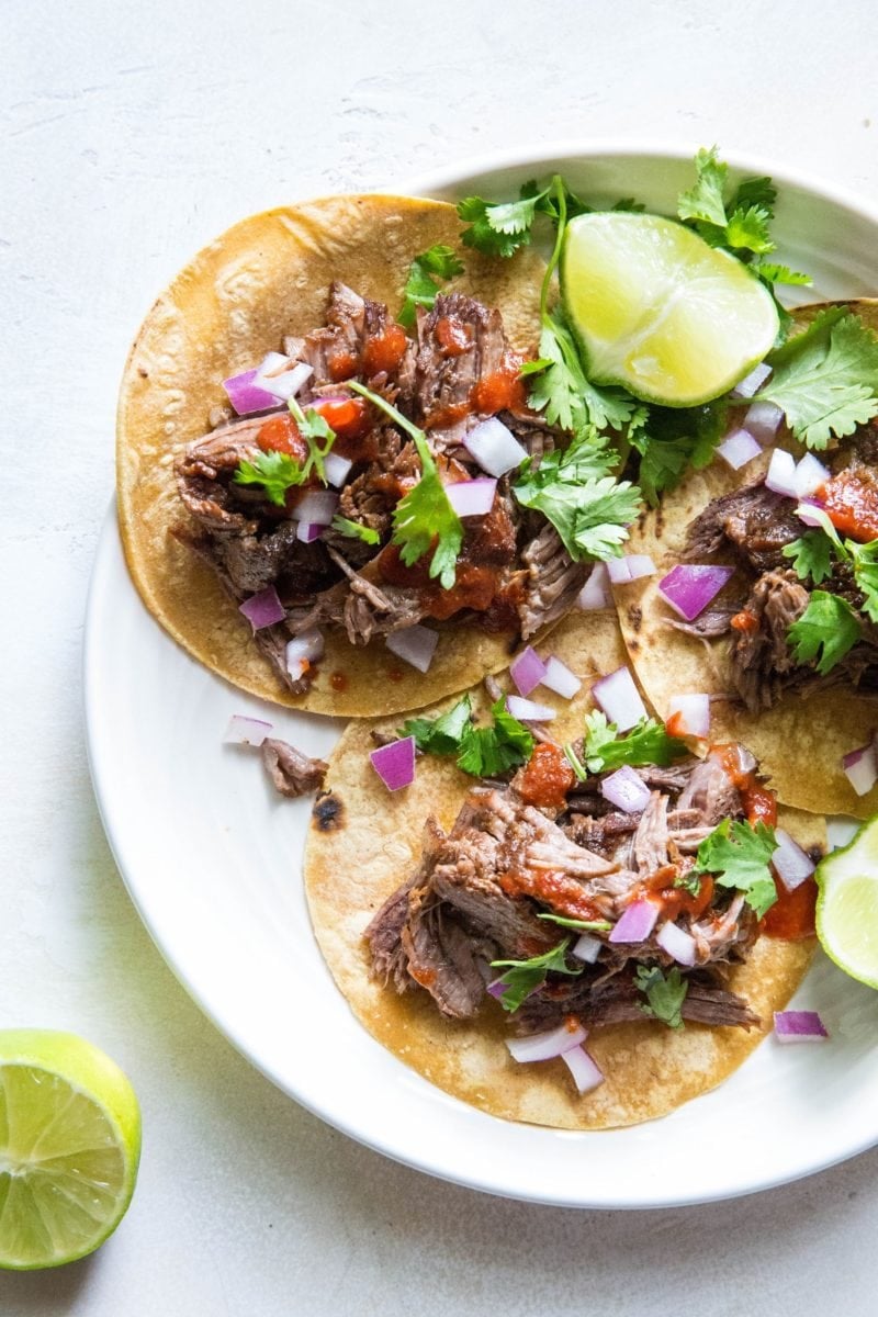 top down photo of beef tacos with red onions, cilantro and salsa on top. Fresh limes to the side.