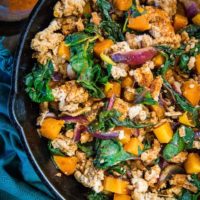 top down photo of cast iron skillet with butternut squash, ground turkey and rainbow chard with a dark blue napkin on a rustic backdrop