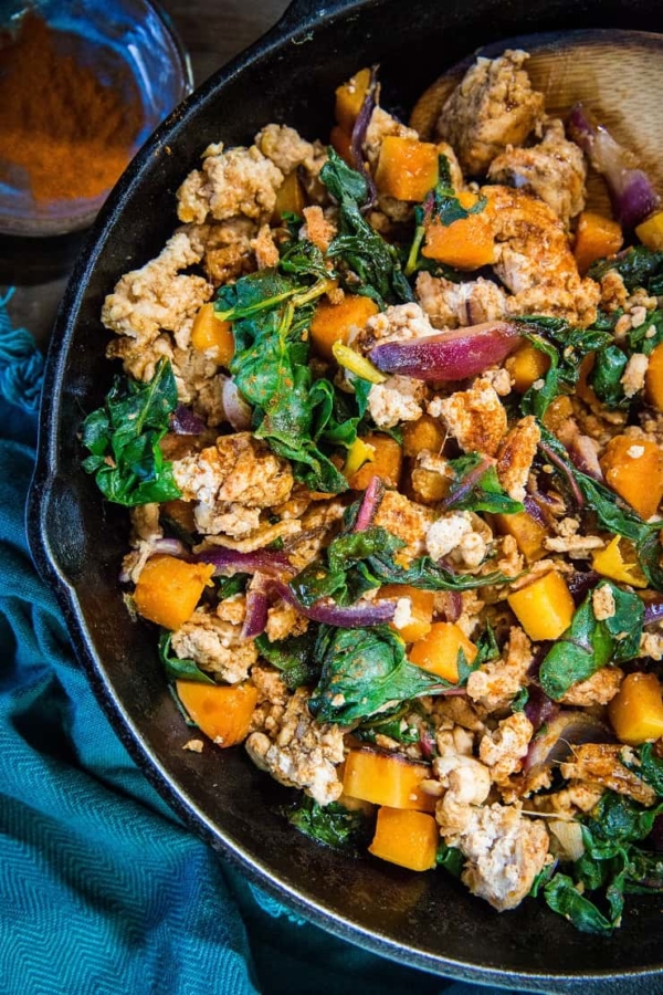 top down photo of cast iron skillet with butternut squash, ground turkey and rainbow chard with a dark blue napkin on a rustic backdrop