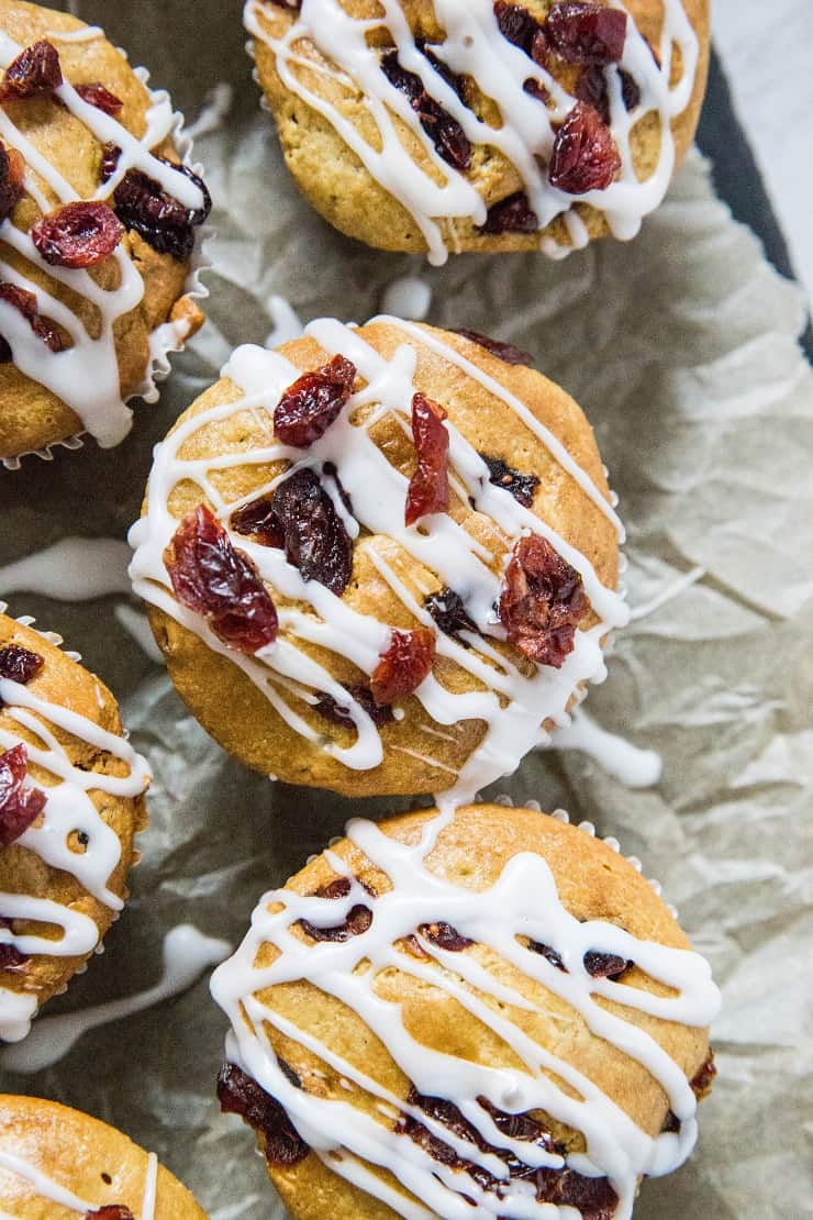 close up top down image of cranberry orange muffins on parchment paper with glaze drizzled on top