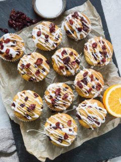 Black stone cutting board with parchment paper and a batch of cranberry orange muffins on top