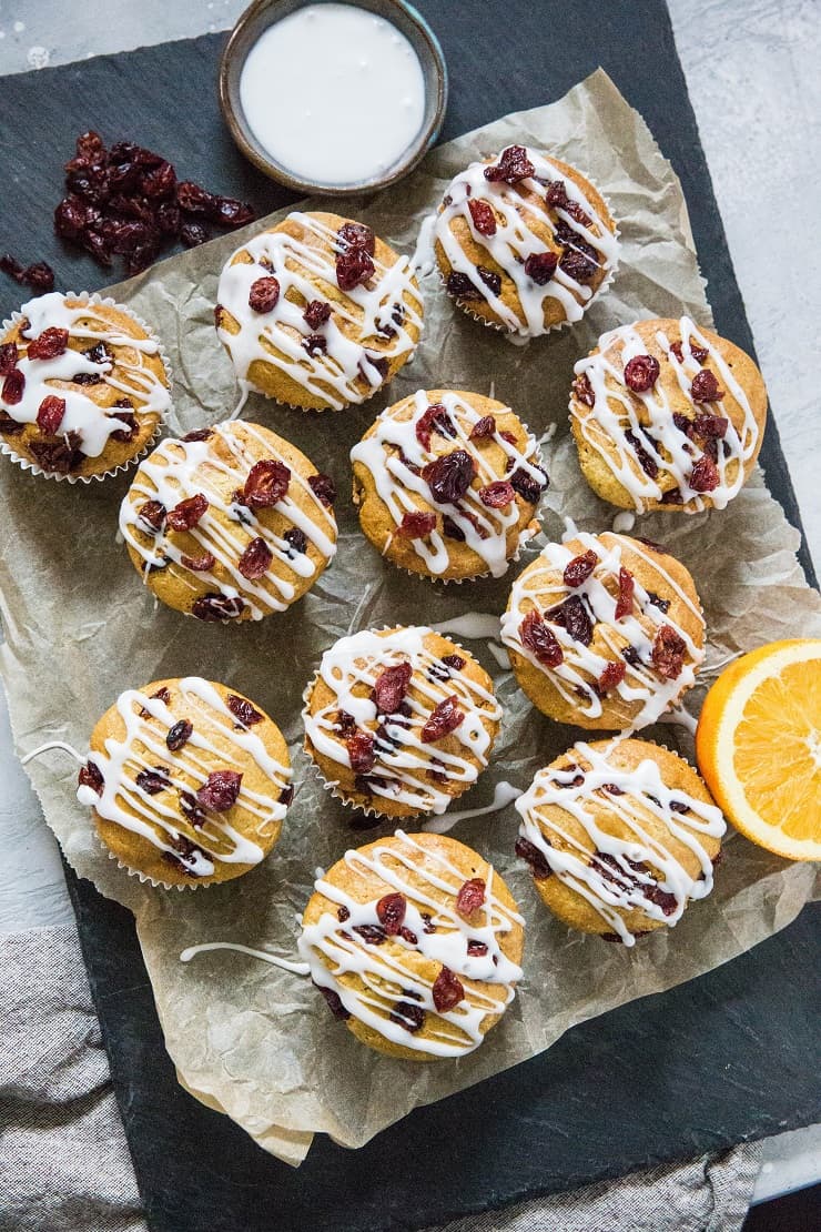 Black stone cutting board with parchment paper and a batch of cranberry orange muffins on top