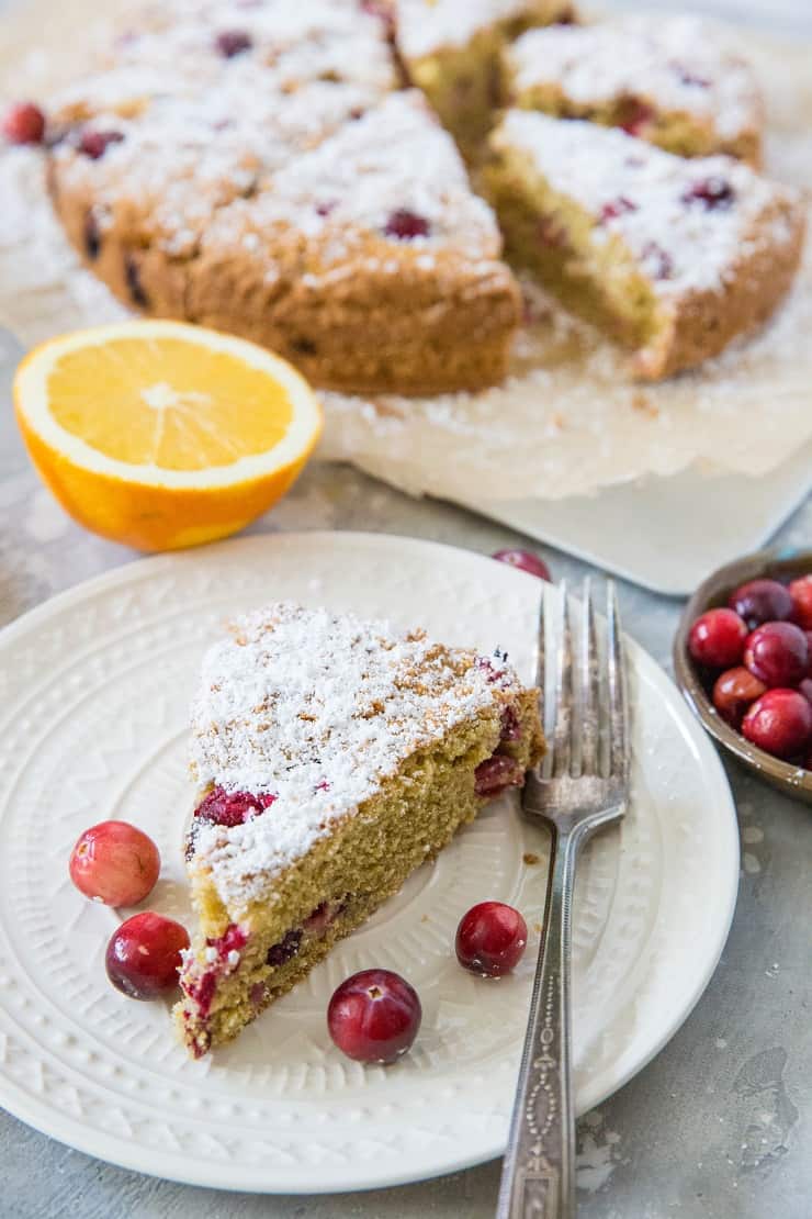 plate with a slice of cranberry orange cake with a fork and fresh cranberries