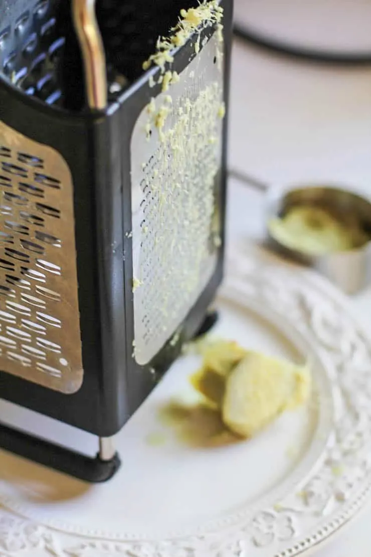 Box grater on a plate with fresh ginger grated on it