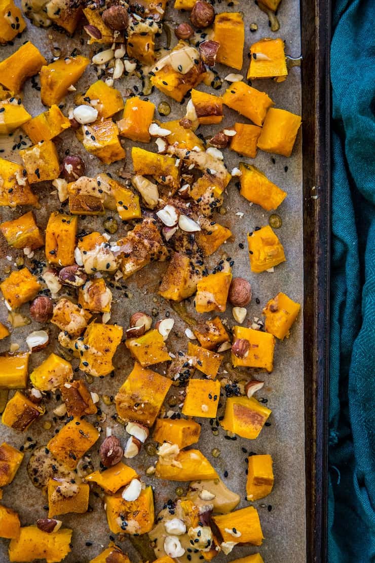 roasted kabocha squash with hazelnuts drizzled with maple tahini on a baking sheet with a dark blue napkin