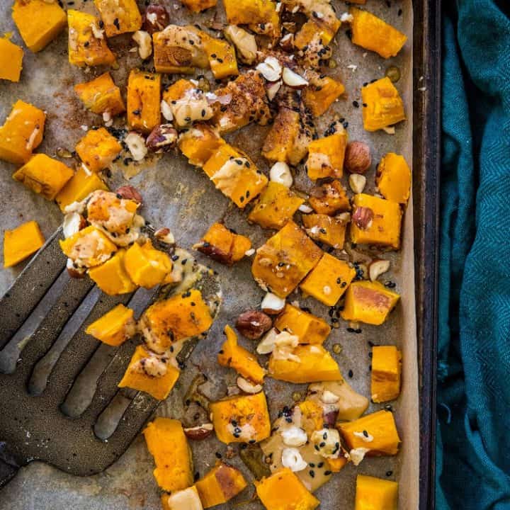 Baking sheet with roasted kabocha squash drizzled in cinnamon tahini with a spatula and dark blue napkin
