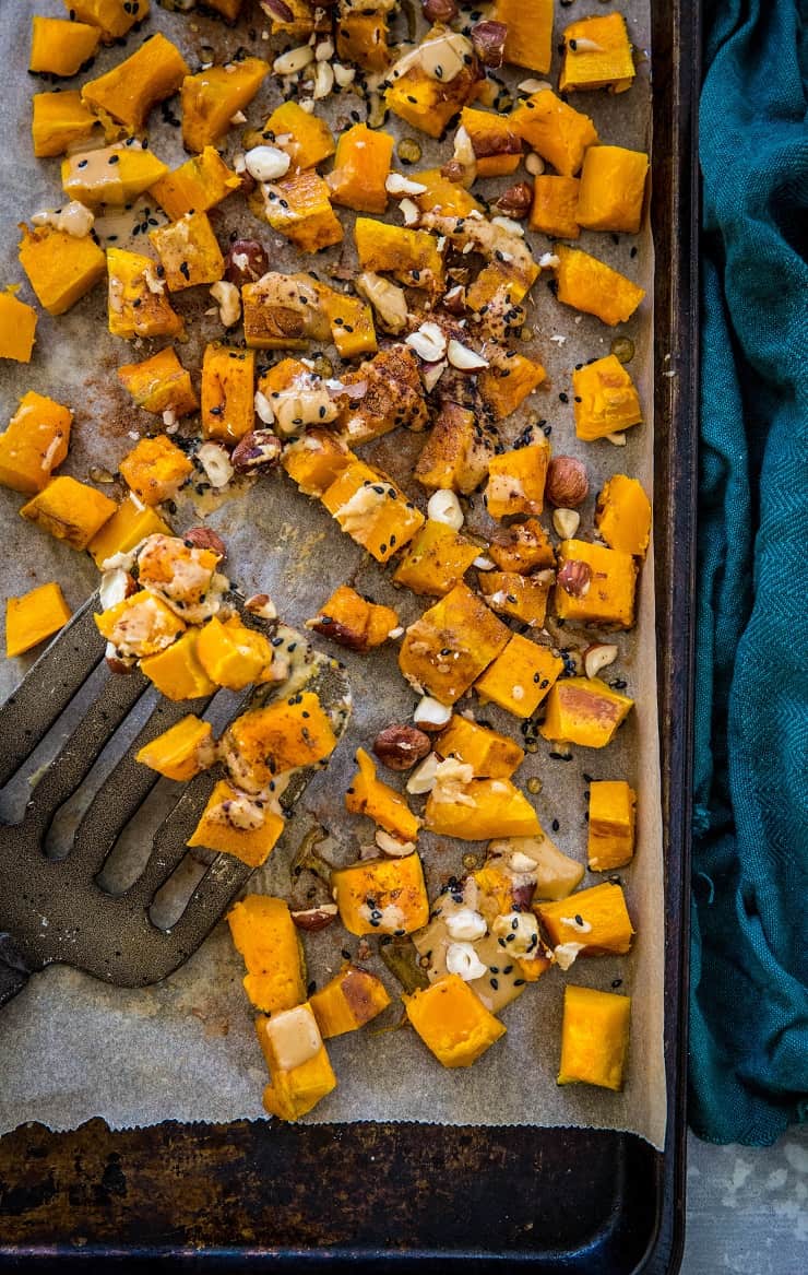 Baking sheet with roasted kabocha squash drizzled in cinnamon tahini with a spatula and dark blue napkin