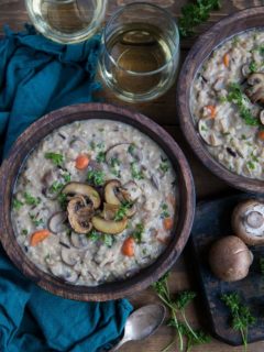 Two wooden bowls of mushroom soup on rustic backdrop with dark blue napkin and two glasses of wine