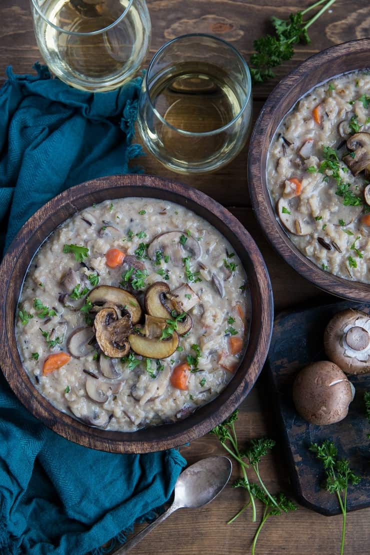 Two wooden bowls of mushroom soup on rustic backdrop with dark blue napkin and two glasses of wine