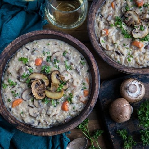 horizontal top down photo of two bowls of vegan mushroom soup with mushrooms and parsley next to bowls on wooden backdrop