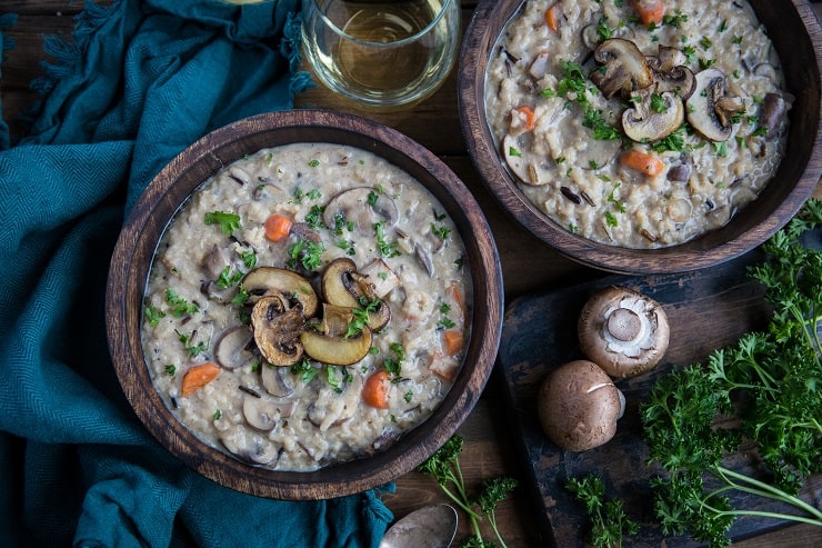 horizontal top down photo of two bowls of vegan mushroom soup with mushrooms and parsley next to bowls on wooden backdrop