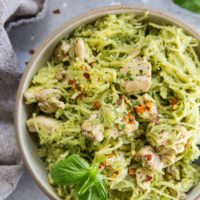 Close up top down image of two bowls of chicken pesto spaghetti squash with basil leaves and red pepper flakes for garnish.