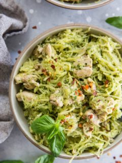 Close up top down image of two bowls of chicken pesto spaghetti squash with basil leaves and red pepper flakes for garnish.