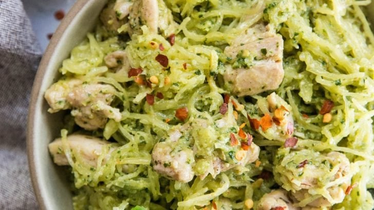 Close up top down image of two bowls of chicken pesto spaghetti squash with basil leaves and red pepper flakes for garnish.