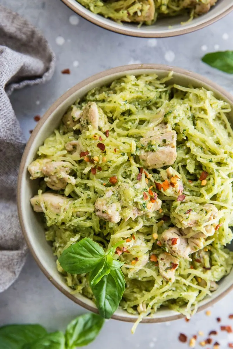 Close up top down image of two bowls of chicken pesto spaghetti squash with basil leaves and red pepper flakes for garnish.