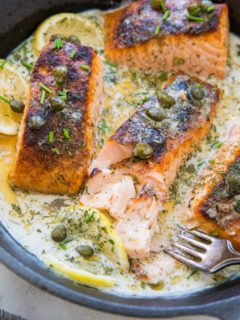 Cast iron skillet with cooked crispy salmon and a creamy dill sauce inside.