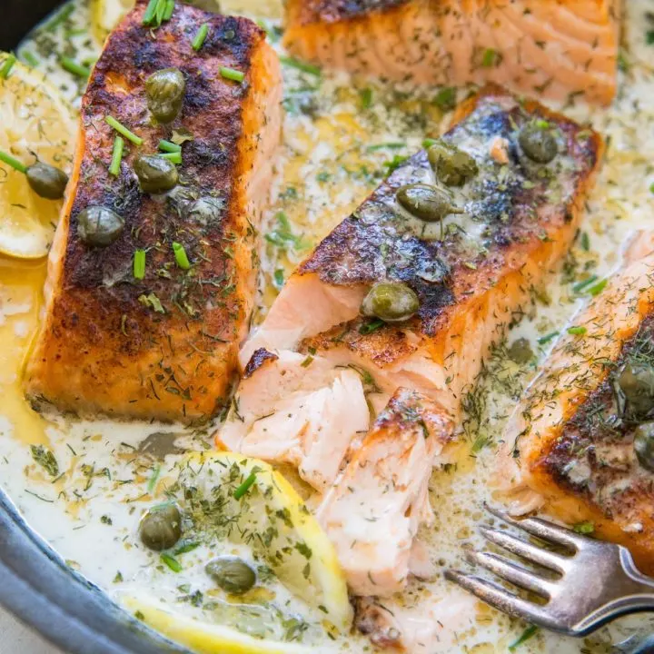 Cast iron skillet with cooked crispy salmon and a creamy dill sauce inside.