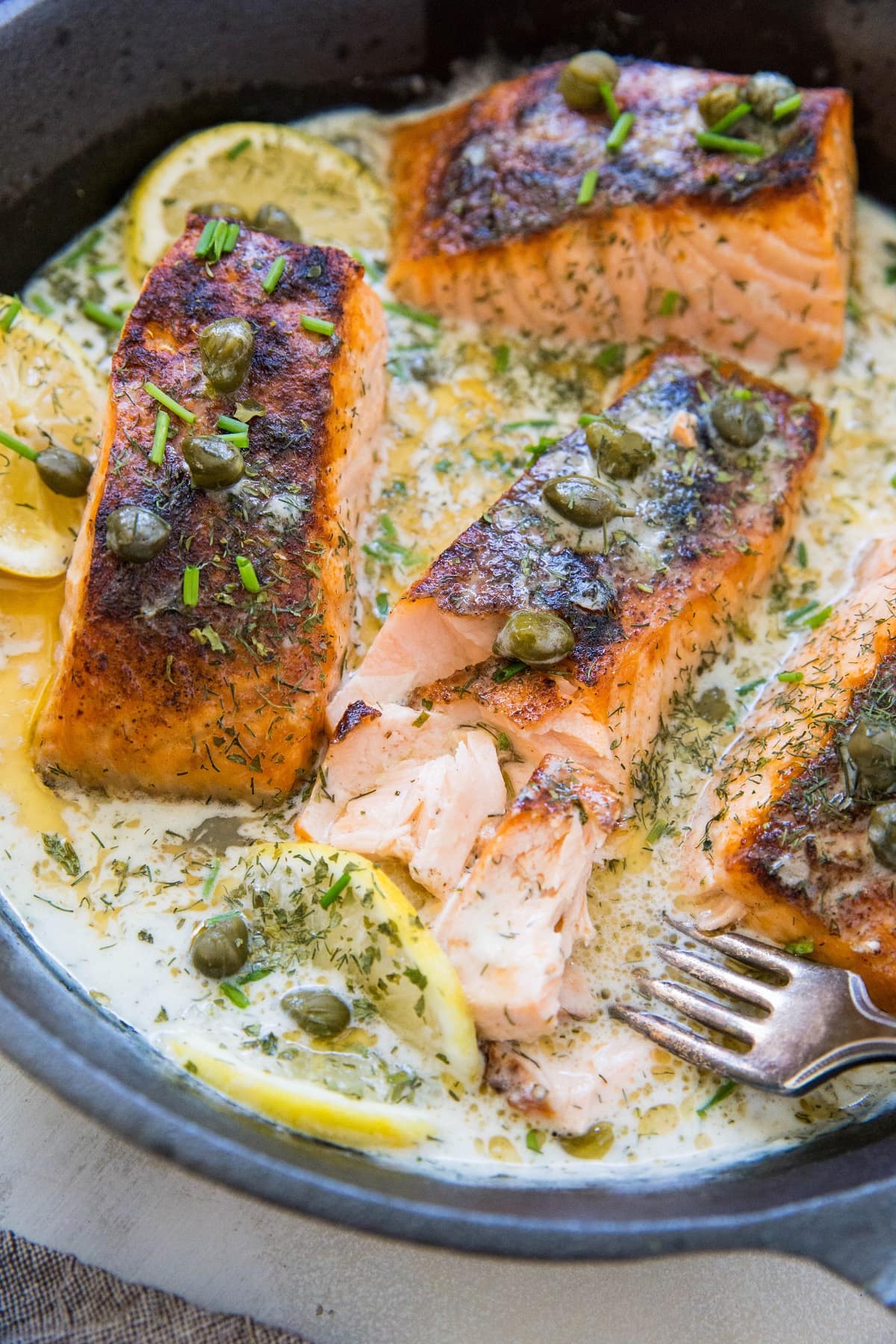 Cast iron skillet with cooked crispy salmon and a creamy dill sauce inside.