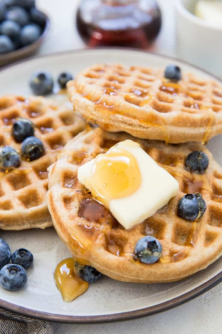 Stack of the best gluten-free waffles on a plate with butter, honey and blueberries