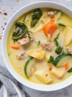 Top down photo of a big bowl of hearty ground turkey soup with grey striped napkin and fresh garlic to the side