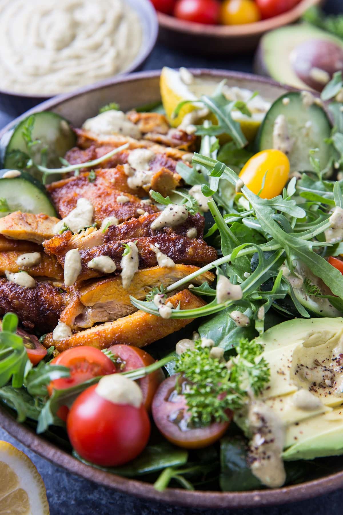 Close up image of crispy Mediterranean chicken salad with fresh vegetables and dressing on top.