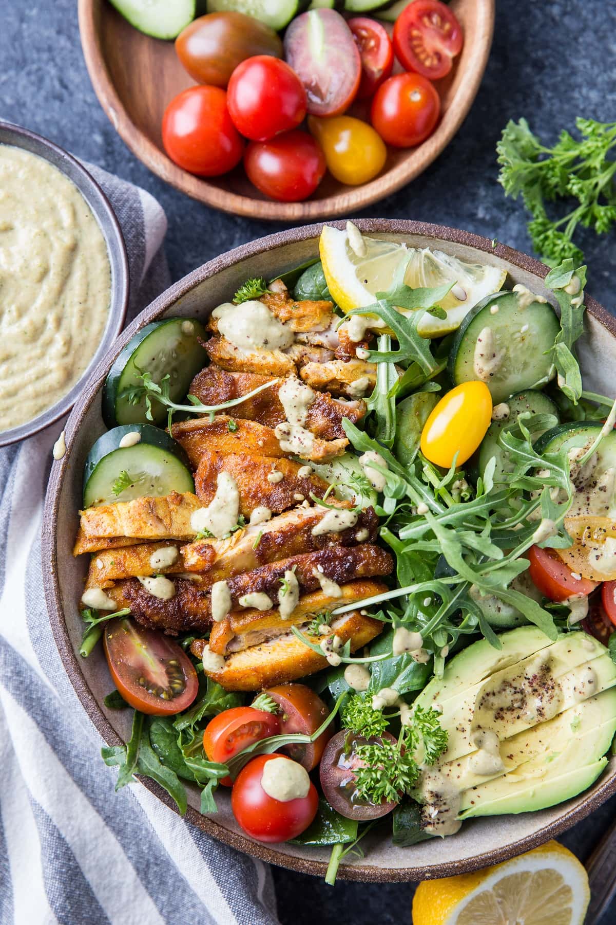 Big bowl of crispy chicken arugula salad with lemon tahini dressing, cherry tomatoes, avocado and more.