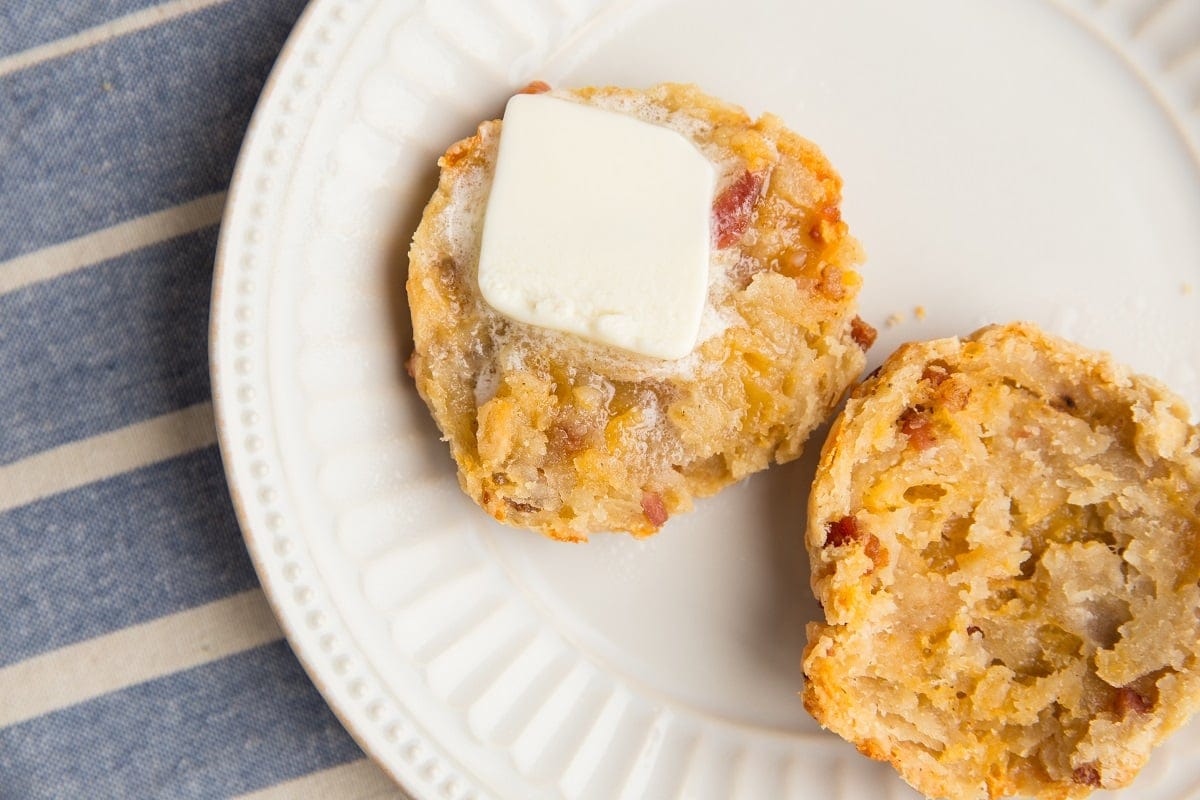 Horizontal image of a gluten-free bacon cheddar biscuit sliced in half with butter on it