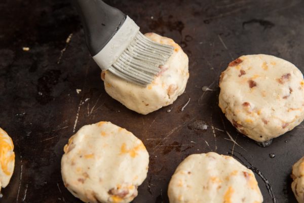 A silicone brush brushing an egg wash onto the biscuit dough.