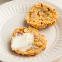 Gluten-Free Bacon Cheddar Biscuit sliced in half on a plate with melted butter on one of the halves and more biscuits on a plate in the background