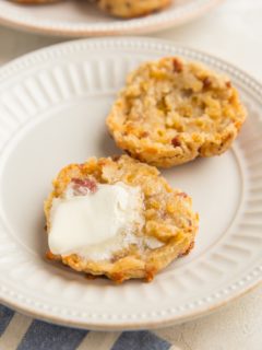 Gluten-Free Bacon Cheddar Biscuit sliced in half on a plate with melted butter on one of the halves and more biscuits on a plate in the background