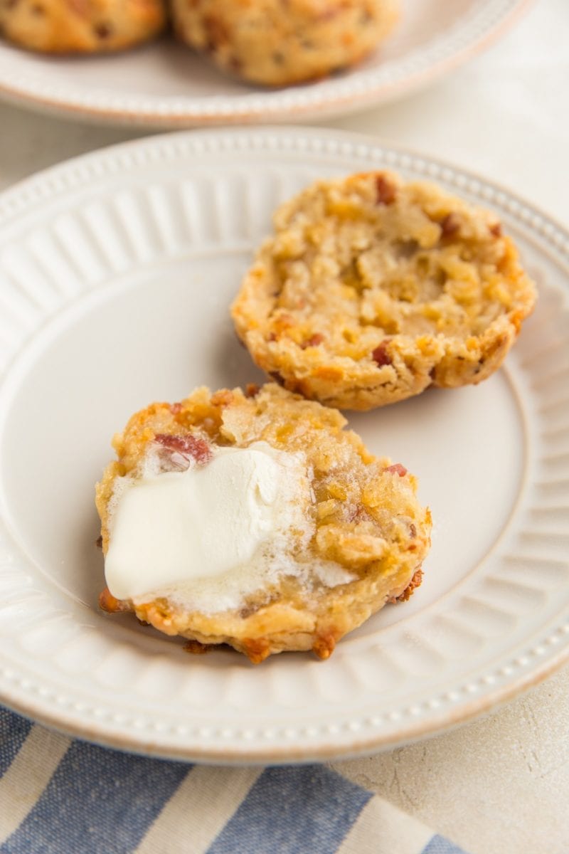 Gluten-Free Bacon Cheddar Biscuit sliced in half on a plate with melted butter on one of the halves and more biscuits on a plate in the background