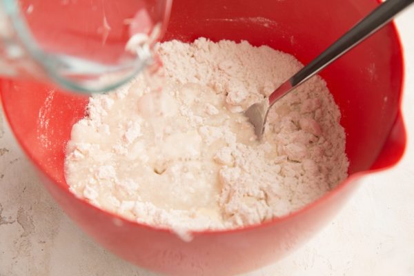 Water being poured in the mixing bowl with the flour