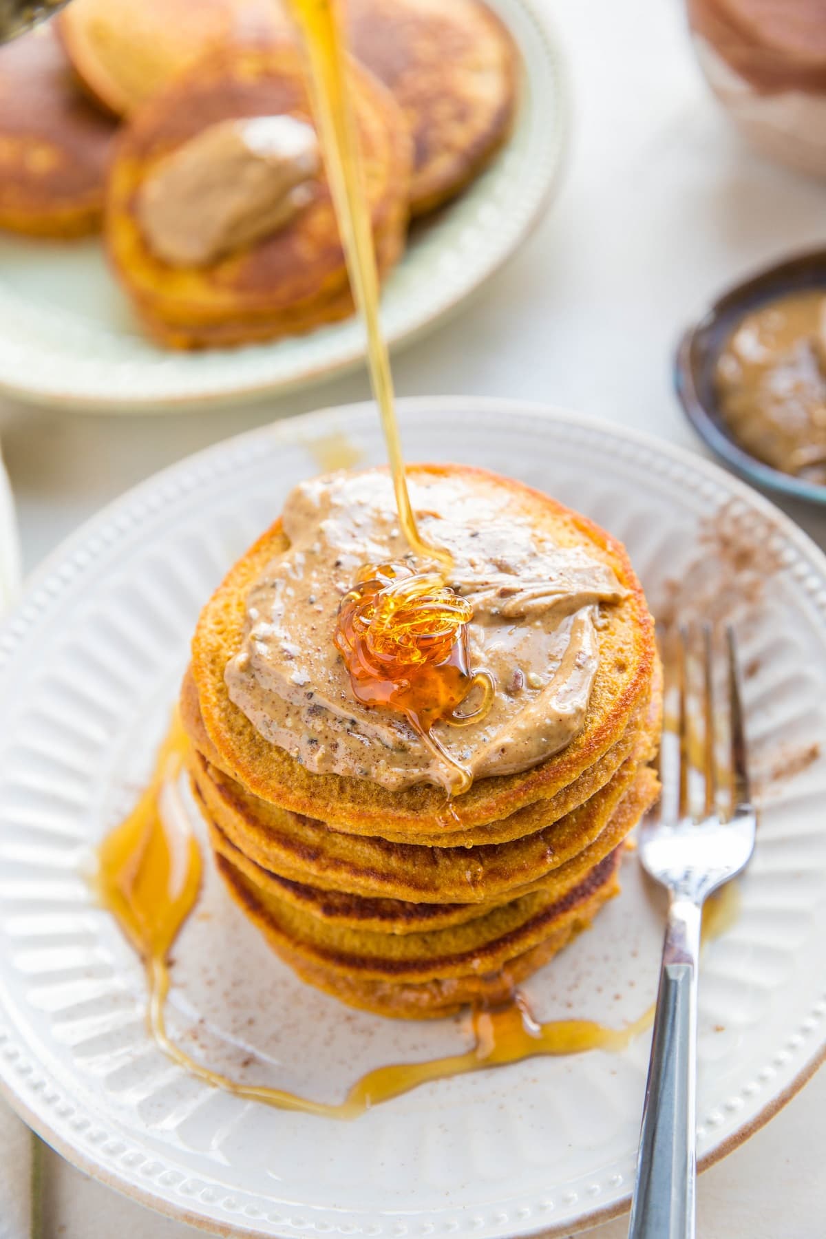 sweet potato pancakes with nut butter on top and honey being poured on top