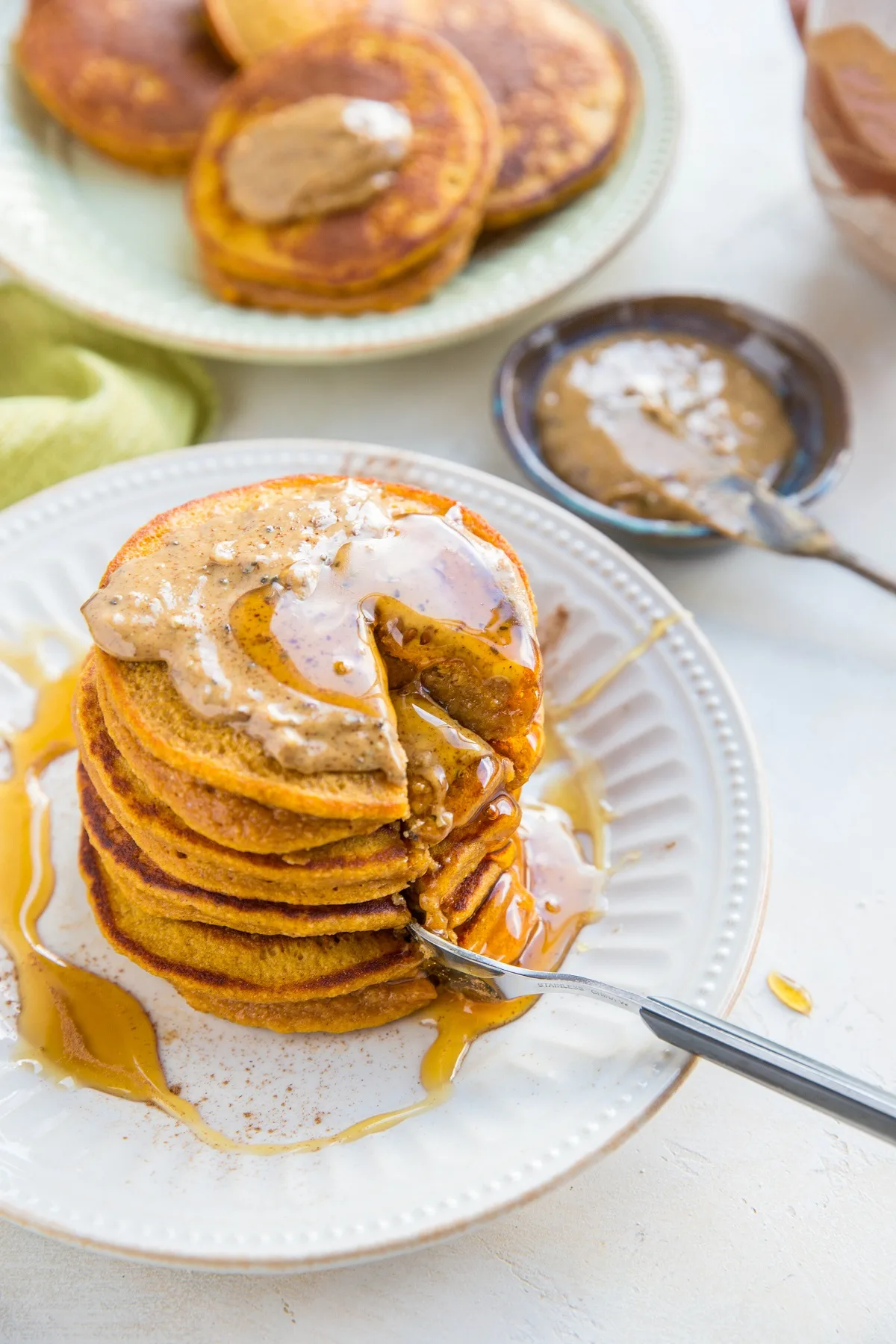 top down photo of stack of sweet potato pancakes with almond butter, honey and a section taken out