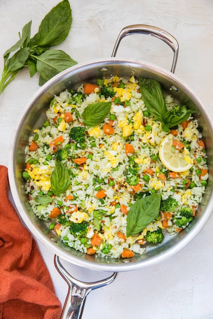 Skillet of basil fried rice on a white backdrop with a red napkin and fresh basil to the side