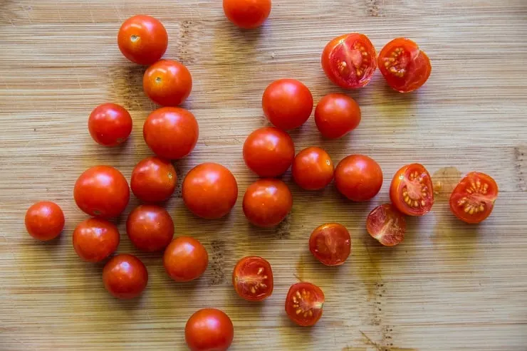Cherry tomatoes chopped in half on a wooden cutting board
