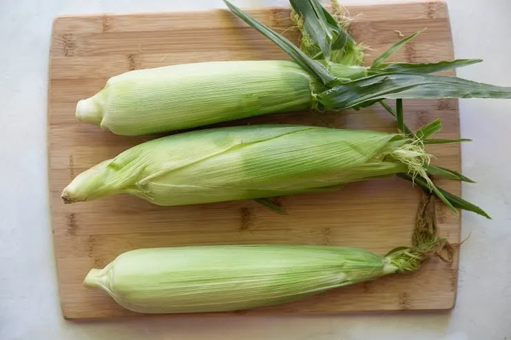 three ears of corn on a wooden cutting board
