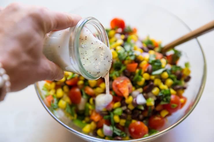 Pouring lemon poppy seed dressing over corn salad