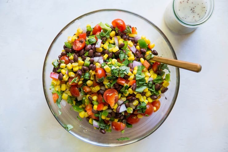 black bean corn salad ingredients in a mixing bowl with lemon poppy seed dressing on the side