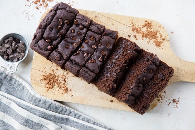 Horizontal photo of black bean banana bread on a cutting board with sprinkles of cocoa powder around