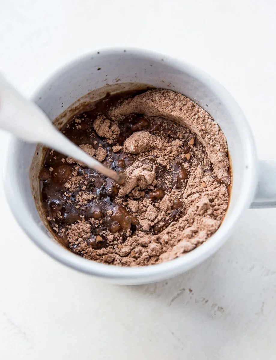 wet ingredients and dry ingredients being stirred together in a mug to make a single serve mug brownie