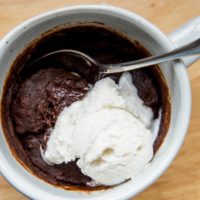 Top down close up photo of a mug brownie with a small scoop of vanilla ice cream on top.