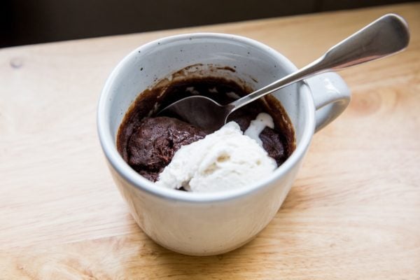 Horizontal image of a mug of brownie and ice cream sitting on a wooden table.